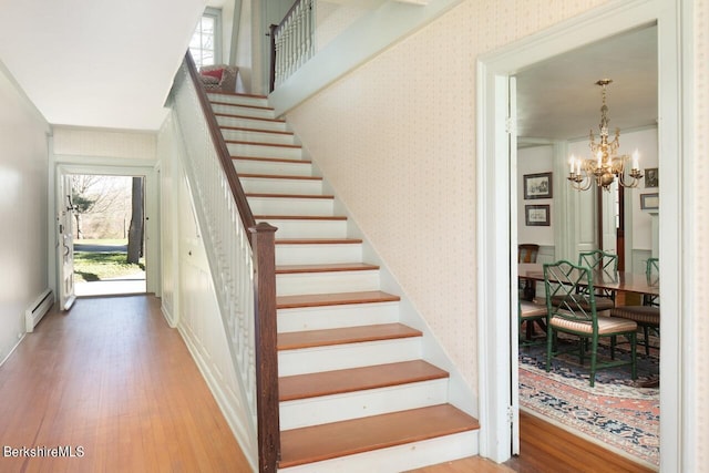 stairs featuring hardwood / wood-style floors, a notable chandelier, ornamental molding, and baseboard heating