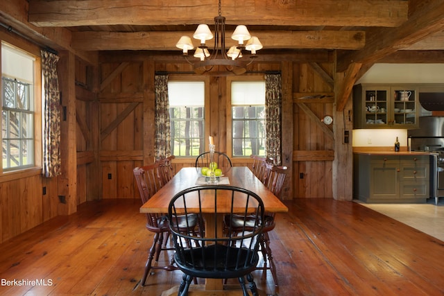 dining room with a notable chandelier, wood walls, light hardwood / wood-style floors, and beam ceiling