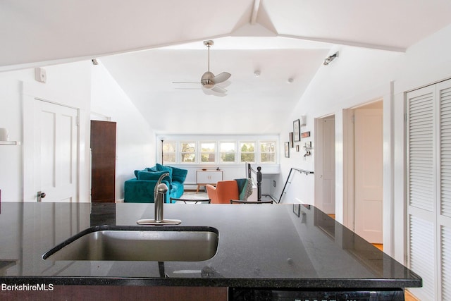 kitchen featuring open floor plan, ceiling fan, dark stone counters, a sink, and vaulted ceiling