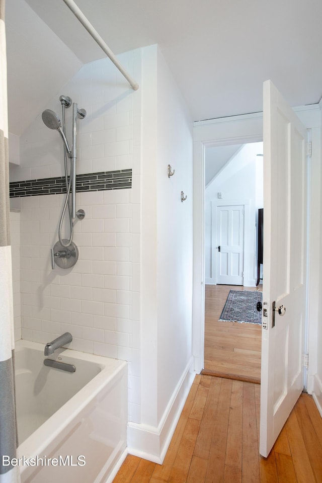 bathroom with baseboards, vaulted ceiling, bathtub / shower combination, and hardwood / wood-style floors