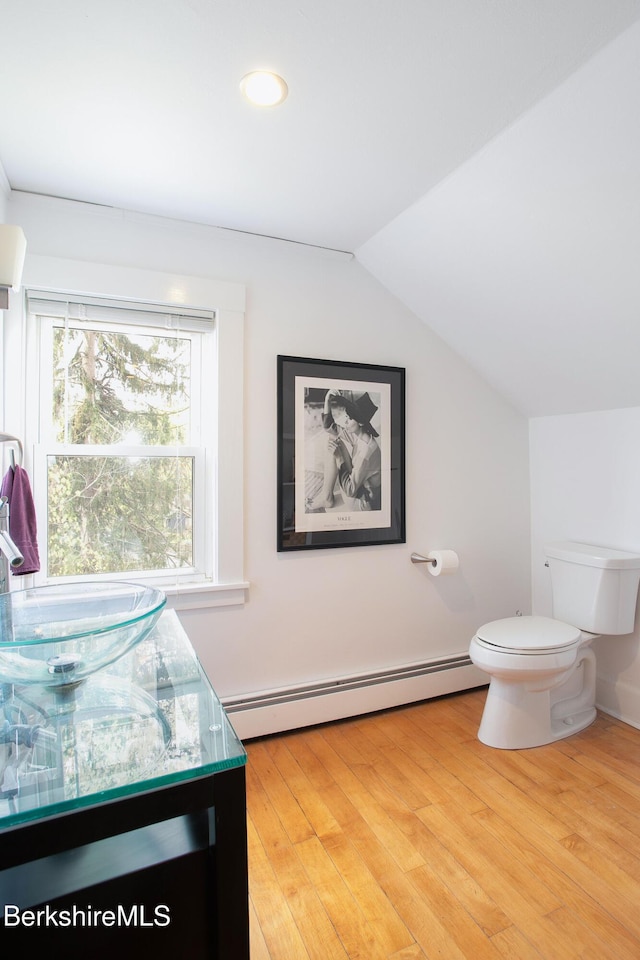 half bathroom featuring vanity, toilet, wood finished floors, a baseboard radiator, and vaulted ceiling