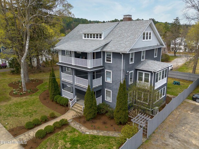 exterior space featuring fence, a shingled roof, a chimney, and a balcony