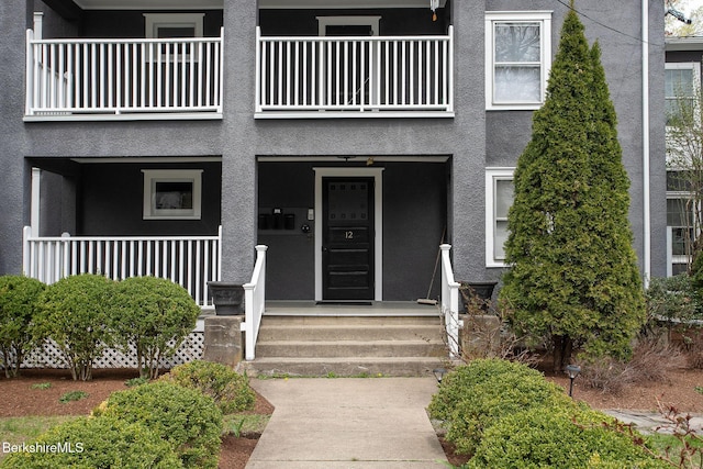 doorway to property with covered porch, stucco siding, and a balcony