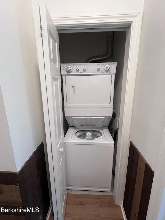 clothes washing area with light hardwood / wood-style flooring and stacked washer / drying machine