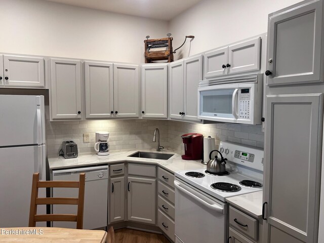 kitchen with white appliances, backsplash, sink, dark hardwood / wood-style floors, and light stone countertops