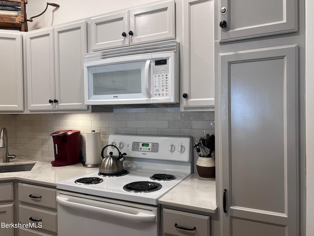 kitchen with decorative backsplash, sink, light stone countertops, and white appliances