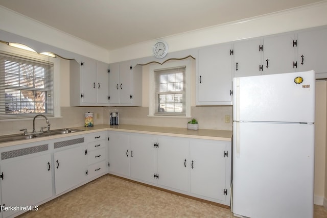 kitchen featuring a sink, backsplash, freestanding refrigerator, white cabinets, and light countertops