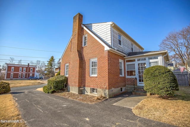 view of home's exterior featuring brick siding, entry steps, a chimney, and fence