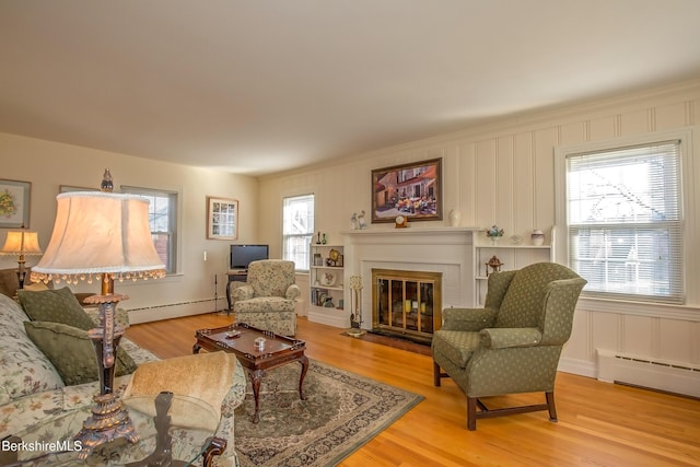 living room with a decorative wall, baseboard heating, light wood-type flooring, and a fireplace with flush hearth