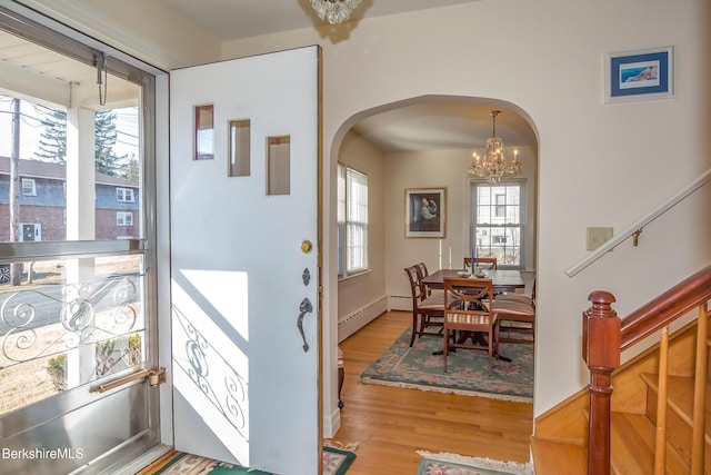 foyer entrance featuring stairway, wood finished floors, a baseboard radiator, arched walkways, and a chandelier