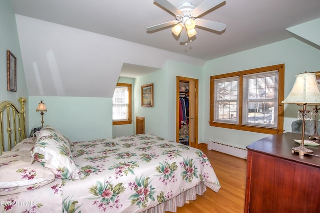 bedroom with a baseboard radiator, multiple windows, a closet, and wood finished floors