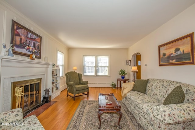 living area featuring a fireplace with flush hearth, wood finished floors, arched walkways, a baseboard radiator, and baseboard heating