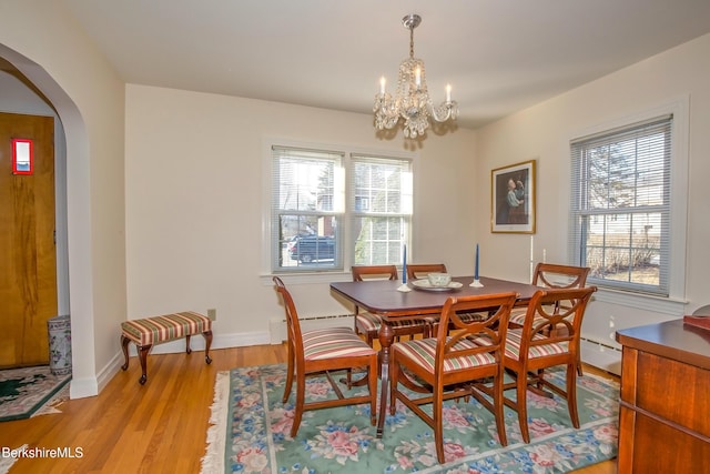 dining area featuring a wealth of natural light, arched walkways, light wood-style floors, and an inviting chandelier
