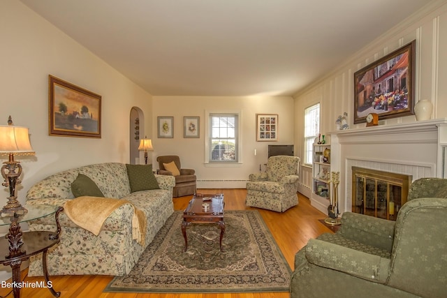 living area featuring a fireplace, wood finished floors, arched walkways, and a baseboard radiator