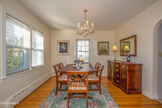 dining space featuring baseboards, a baseboard radiator, arched walkways, light wood-style floors, and a notable chandelier
