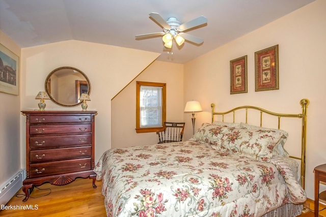 bedroom with ceiling fan, a baseboard radiator, wood finished floors, and vaulted ceiling