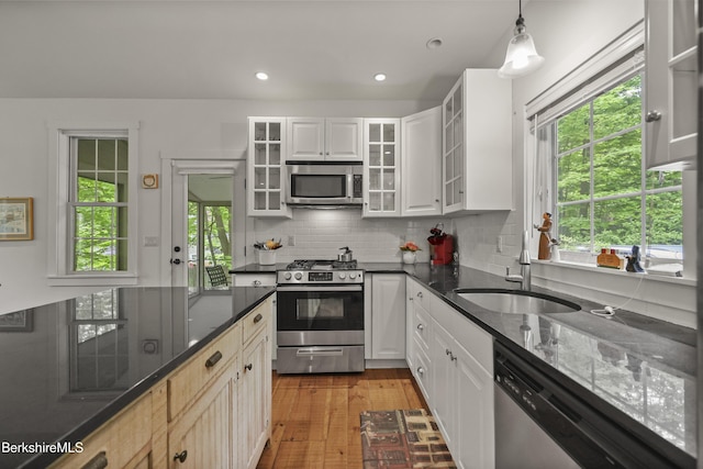 kitchen with appliances with stainless steel finishes, a sink, tasteful backsplash, light wood finished floors, and dark stone counters