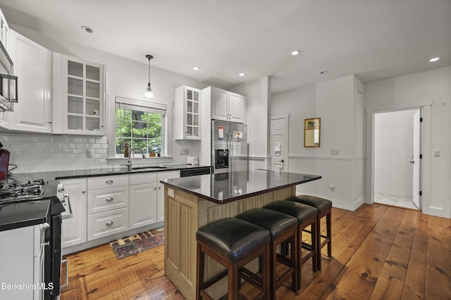 kitchen with stainless steel fridge with ice dispenser, gas range oven, dark countertops, wood-type flooring, and a wainscoted wall
