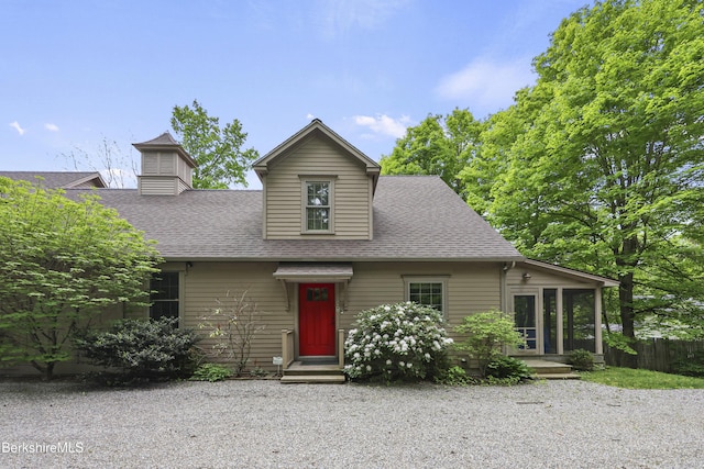 view of front facade featuring a shingled roof, fence, and a sunroom