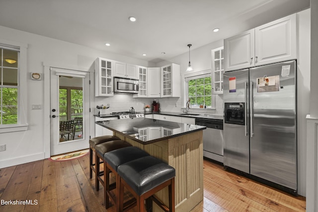 kitchen with appliances with stainless steel finishes, a sink, light wood-type flooring, dark countertops, and recessed lighting