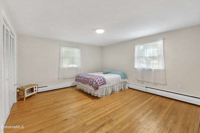 bedroom featuring a closet, light hardwood / wood-style flooring, and a baseboard heating unit