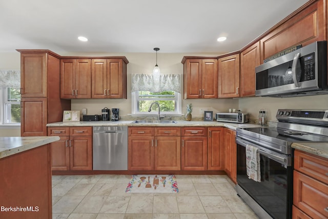 kitchen featuring appliances with stainless steel finishes, light stone counters, pendant lighting, and sink