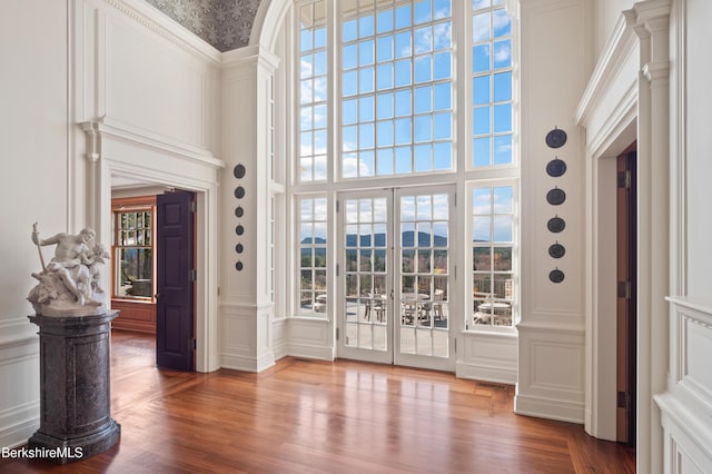 interior space featuring french doors, decorative columns, wood-type flooring, a mountain view, and a high ceiling