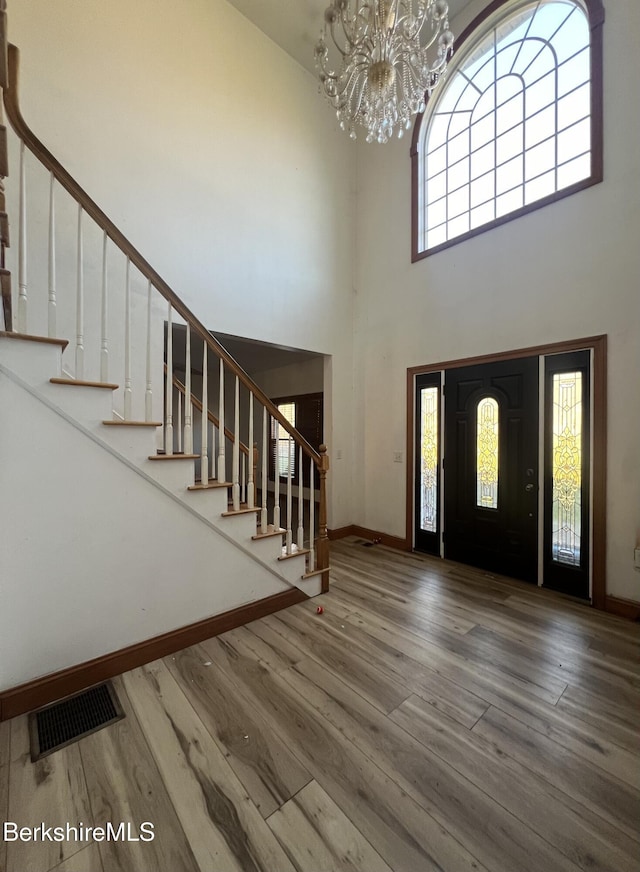 foyer entrance with wood-type flooring, a towering ceiling, and a notable chandelier