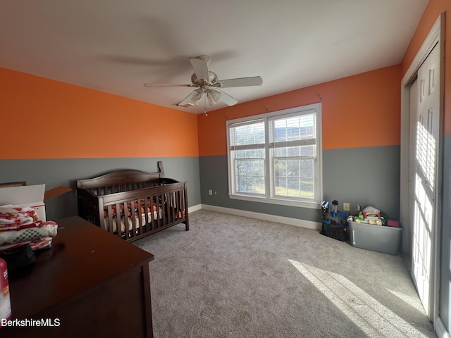 bedroom featuring a crib, light carpet, a closet, and ceiling fan