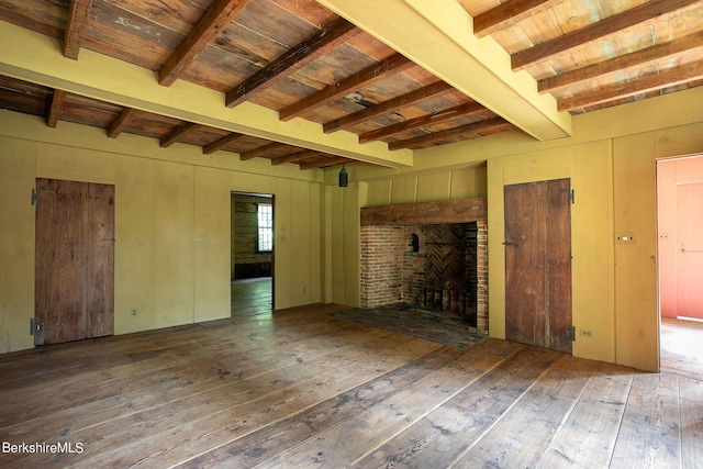 unfurnished living room with a fireplace, beamed ceiling, and wood-type flooring