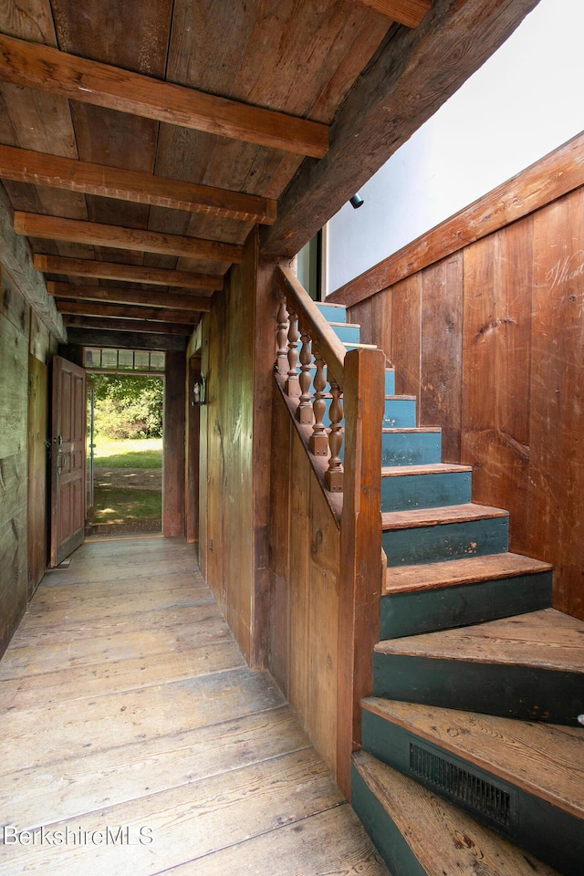 stairway featuring wooden ceiling, wooden walls, beamed ceiling, and wood-type flooring