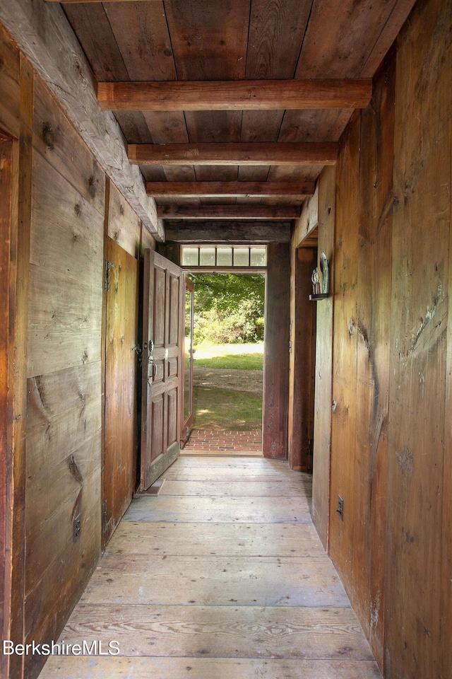 corridor with beam ceiling, light hardwood / wood-style floors, wooden walls, and wood ceiling