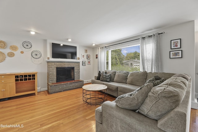 living room featuring a baseboard radiator, baseboards, a stone fireplace, and light wood finished floors