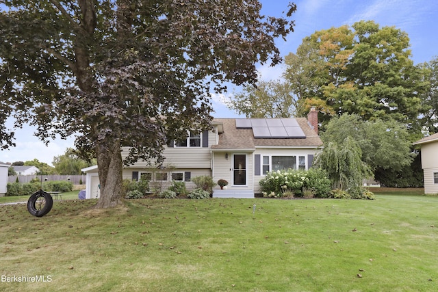 tri-level home featuring a front lawn, roof mounted solar panels, an attached garage, a shingled roof, and a chimney