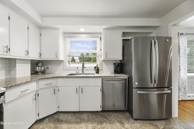 kitchen with light stone counters, a sink, appliances with stainless steel finishes, white cabinetry, and tasteful backsplash