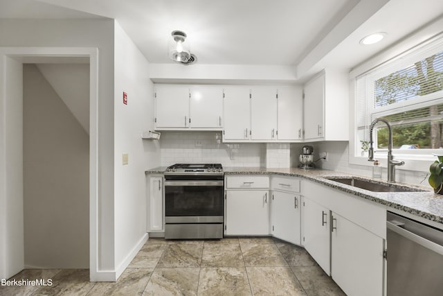 kitchen featuring a sink, light stone counters, white cabinetry, appliances with stainless steel finishes, and decorative backsplash