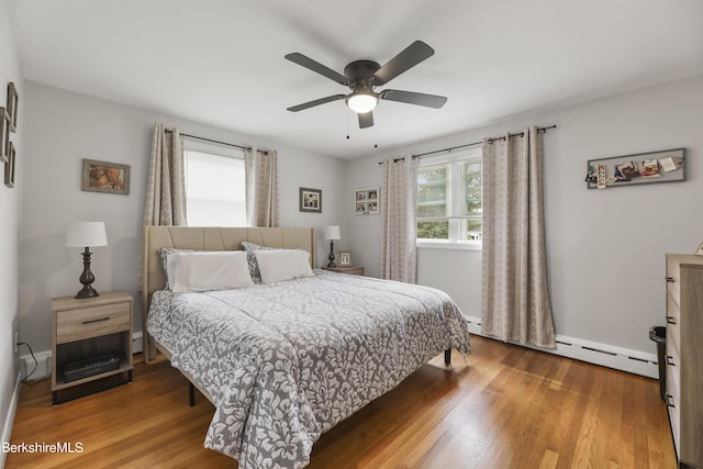 bedroom featuring a baseboard heating unit, wood finished floors, baseboards, and ceiling fan