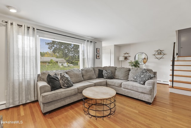 living room featuring stairs, light wood finished floors, and a baseboard radiator