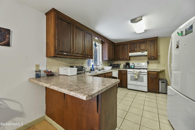 kitchen featuring white appliances, a peninsula, light tile patterned flooring, a sink, and under cabinet range hood