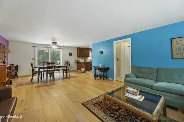 living area featuring light wood finished floors, baseboards, and ceiling fan