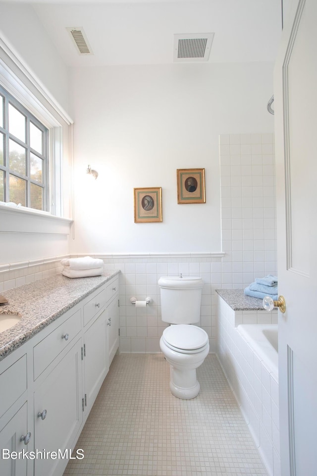 bathroom with a tub, tile patterned flooring, toilet, vanity, and tile walls