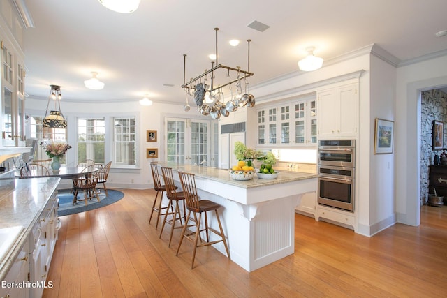 kitchen with double oven, white cabinetry, a center island, and pendant lighting