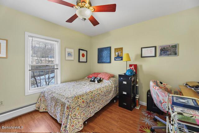 bedroom with a baseboard heating unit, a ceiling fan, and wood finished floors