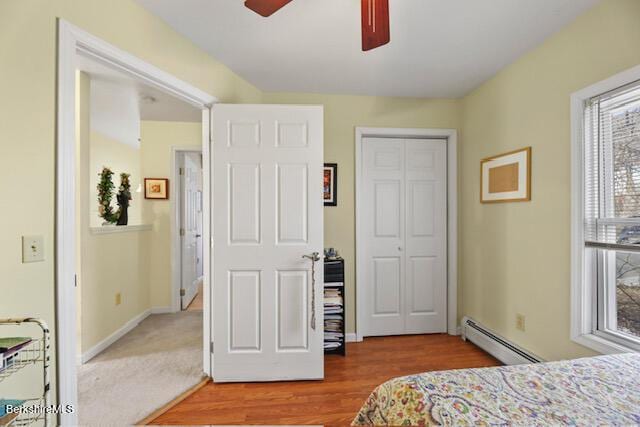 bedroom featuring a baseboard heating unit, wood finished floors, a closet, baseboards, and ceiling fan