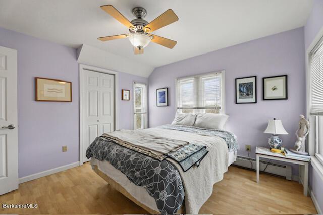 bedroom featuring light wood finished floors, baseboards, a closet, and a baseboard radiator