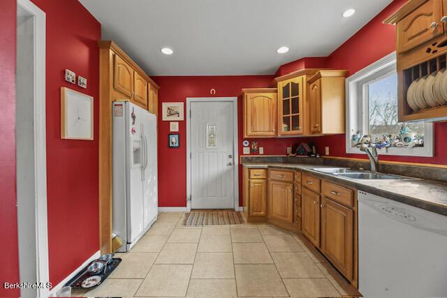 kitchen with a sink, white appliances, brown cabinetry, light tile patterned floors, and glass insert cabinets