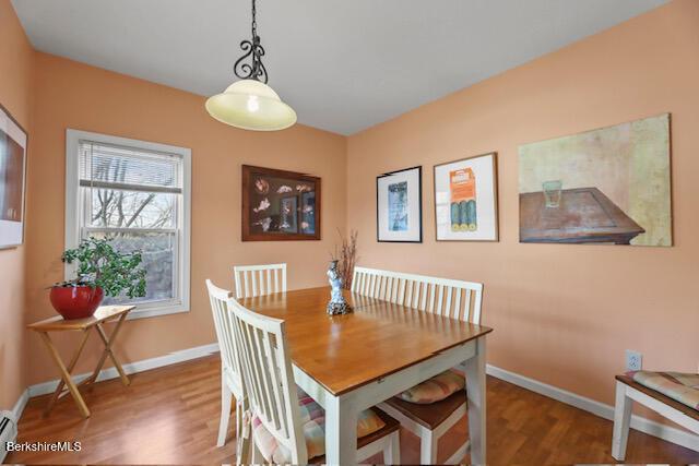 dining space featuring a baseboard heating unit, baseboards, and wood finished floors