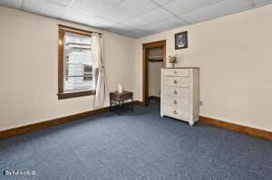 unfurnished bedroom featuring a drop ceiling and dark carpet