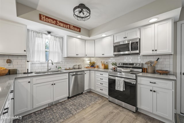 679 Middle Pownal Rd, Pownal, VT 05261 - kitchen with appliances with stainless steel finishes, light wood-style floors, white cabinetry, decorative backsplash, and light countertops