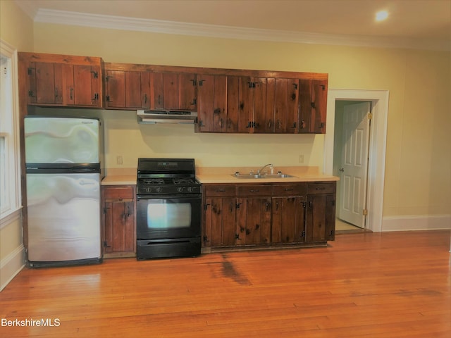 kitchen featuring black gas stove, a sink, light countertops, under cabinet range hood, and freestanding refrigerator
